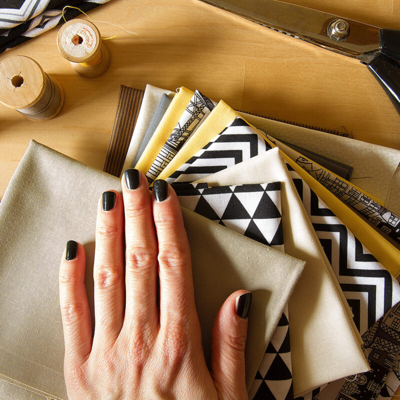 Hand with dark nail varnish held over fabric pile of various fashions